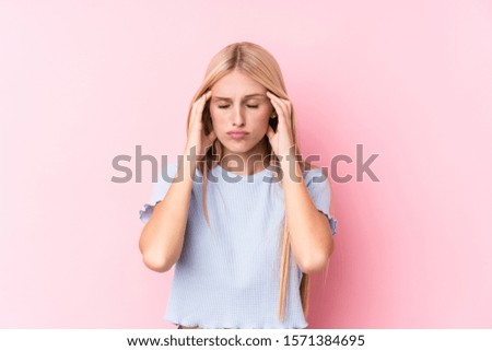 Young blonde woman on pink background touching temples and having headache.