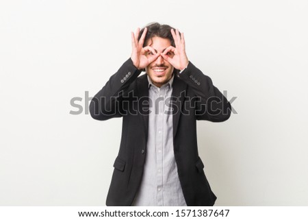 Young business man against a white background showing okay sign over eyes