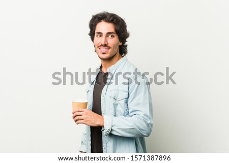 Young cool man drinking a coffee looks aside smiling, cheerful and pleasant.