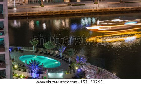 Waterfront promenade with swimming pool in Dubai Marina aerial night timelapse. Boats and yachts floating on canal. Dubai, United Arab Emirates