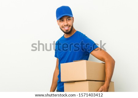 Young south-asian delivery man looks aside smiling, cheerful and pleasant.