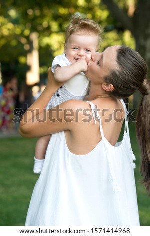 Young mother walks with her little son in the Park in the summer. Happy loving young mother kisses her son on the walk.