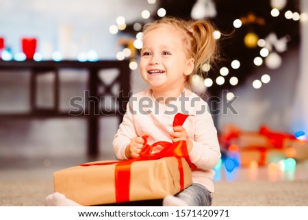 Cute happy little girl opening Christmas gift at home, empty space