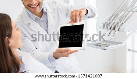 Cropped image of dentist showing patient blank digital tablet screen, dental clinic, panorama