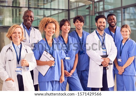 Portrait Of Smiling Medical Team Standing In Modern Hospital Building Royalty-Free Stock Photo #1571429566