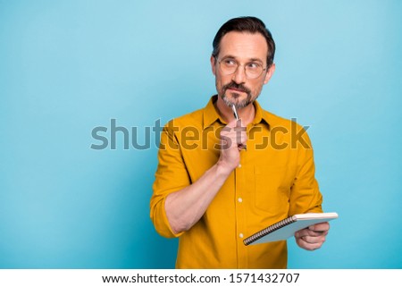 Portrait of serious focused man write essay in his copy book think thoughts contemplate wear modern clothes isolated over blue color background Royalty-Free Stock Photo #1571432707