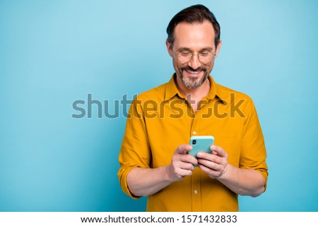 Portrait of cheerful attractive mature man modern device user use his smart phone type social network message wear good looking clothes isolated over blue color background