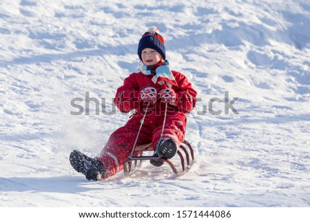 happy boy sitting at the sledge on snowy hill, winter holidays concept