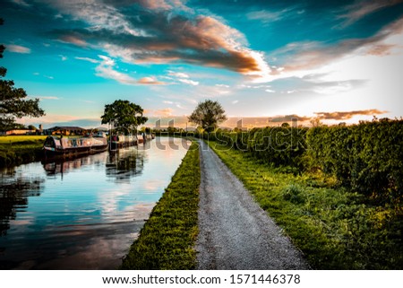 Cheshire Countryside Canal scene, with barges, trees and farm fields set in the Uk summertime at sunset. Royalty-Free Stock Photo #1571446378