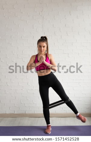 An athlete in top and leggings performs exercises for the leg muscles with a fitness elastic band.