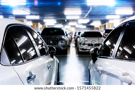Two White cars in a parking lot with blur background of many cars and shining neon light