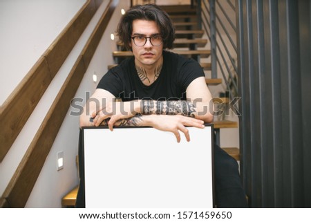 Man holding a picture frame or poster for mock up wearing black clothes in a room interior