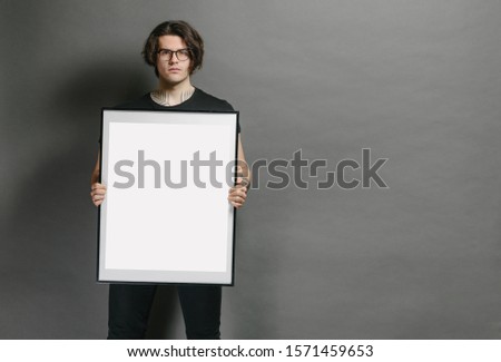 Man holding a picture frame or poster for mock up wearing black clothes