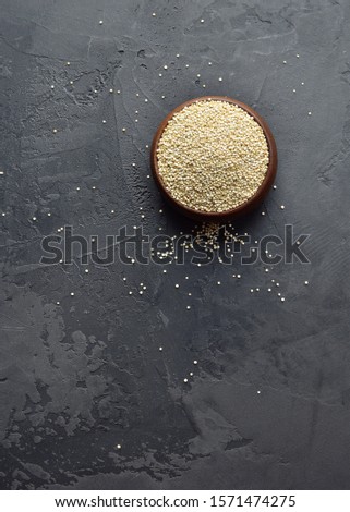 Dry organic quinoa seeds in wooden bowl on dark grunge background, vertical top view, copy space