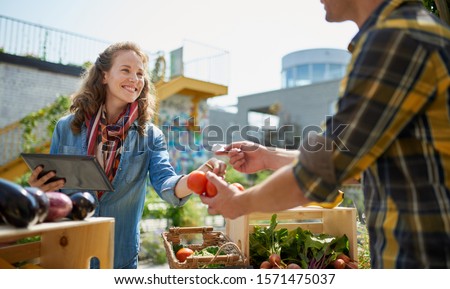 Friendly woman tending an organic vegetable stall at a farmer's Royalty-Free Stock Photo #1571475037