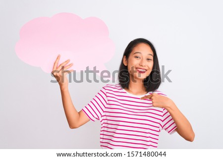 Young chinese woman holding cloud speech bubble standing over isolated white background with surprise face pointing finger to himself