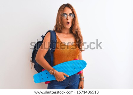 Young redhead student woman wearing backpack and skateboard over isolated background scared in shock with a surprise face, afraid and excited with fear expression