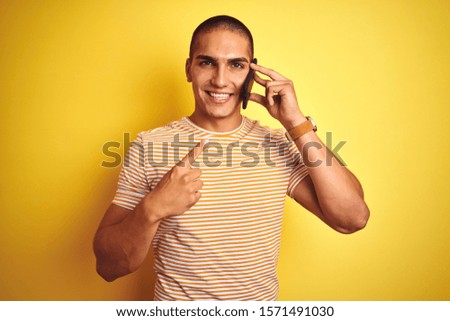 Young handsome man talking using smartphone over yellow isolated background very happy pointing with hand and finger