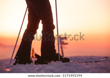 Close Up photo of female skiers legs with ski poles against sunset sky