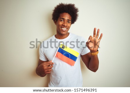 Afro american man holding Venezuela Venezuelan flag standing over isolated white background doing ok sign with fingers, excellent symbol