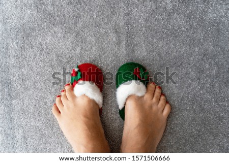 Legs in Christmas red and green slippers are on grey rug, view from the top, new year concept