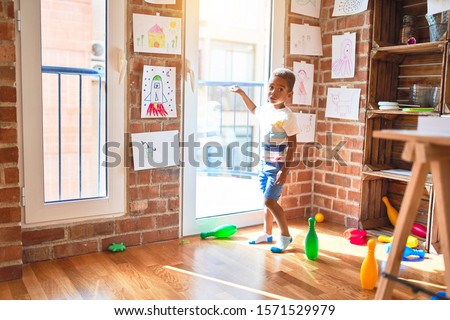 Beautiful african american toddler standing pointing with finger to the window at kindergarten