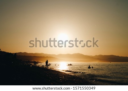 A silhouette of people having fun at the beach with mountains and clear sky in the background