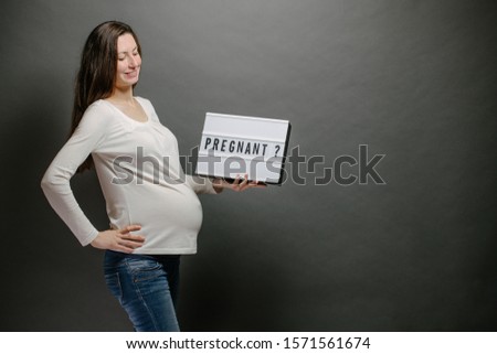 Pregnant woman holding a lightbox with a sign pregnant or pregnancy over gray wall