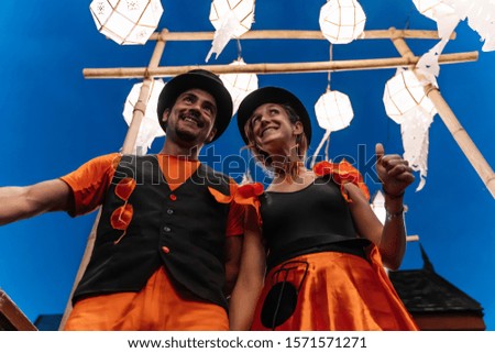 Stock photo of a couple of disguised circus tightrope walkers wearing a hat with out-of-focus Chinese lanterns in the background at night. Lifestyle and nomad