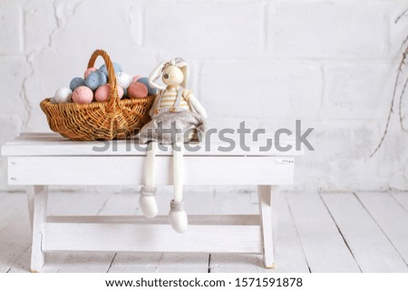 A rabbit is sitting at the Easter basket with colored eggs. Fluffy cute belly - a symbol of Easter. Religious holiday.

