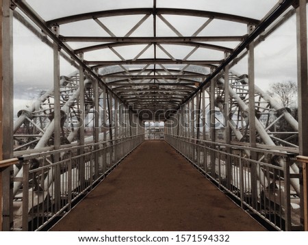 Empty metal bridge for pedestrians with a roof on a moody and cloudy sky background with trees