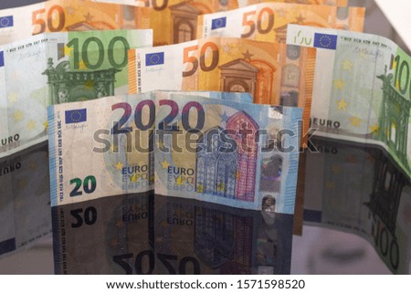 The picture shows the number 2020 made of 20 Euro bills surrounded by currencies coins and bills