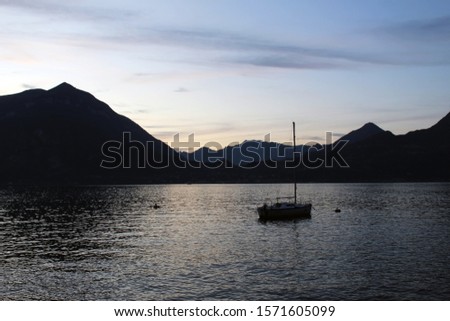 Sailboat floating on a lake surrounded by mountains at sunset