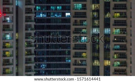 Rows of glowing windows with people in the interior of apartment building at night. Modern skyscraper with glass surface. Concept for business and modern life. Zoom in