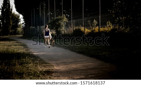 A young lady walking in the park along the pathway with her dog on a beautiful evening