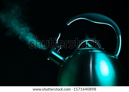 Photo of tainless stell kettle in neon light over dark background. Steam from the kettle through the whistle.
