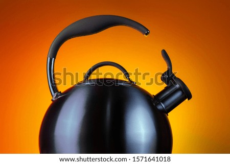 Close-up photo of stainless steel kettle in neon light over orange background.