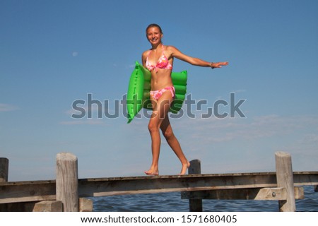 Teenage girl walking along pier holding airbed