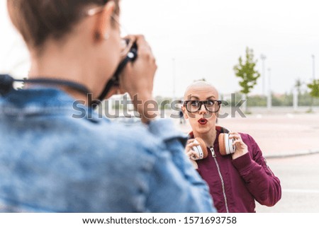 Two Hipster Girls Taking Pictures to Each Other Outdoors. Friend Women Hanging Out in the Street. Two Girls Having Fun Together. Lifestyle Concept.