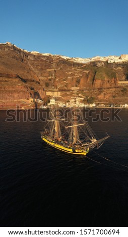 Aerial drone photo of wooden sail boat docked near old port of Santorini island in deep blue sea just below village of Fira, Cyclades, Greece