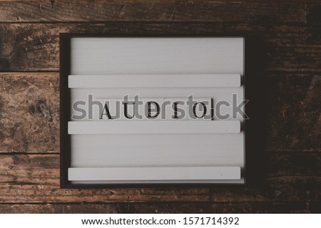 A white sign with a writing "Audio" on it on a wooden brown background