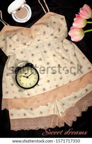 cotton pajamas with lace on a black background with a bouquet of tulips with face powder and an alarm clock. Below the inscription: "sweet dreams" Suitable for advertising.