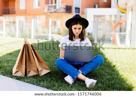 Young woman using computer shopping online sitting on grass. outdoors background.