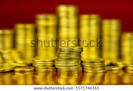 Shiny stack of golden coins. Close up photo. Business concept. Reflection on the table. Red background.