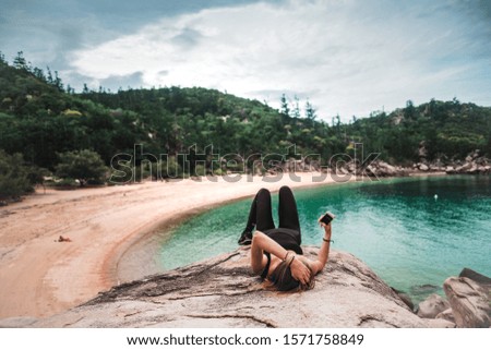 Young girl sitting on the rock with beautiful view on the beach and sea and looking into her phone