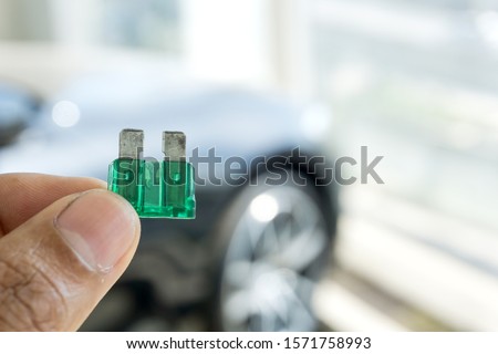 Man hand holding Automotive blown fuse on blurred car in repair shop on background. Royalty-Free Stock Photo #1571758993