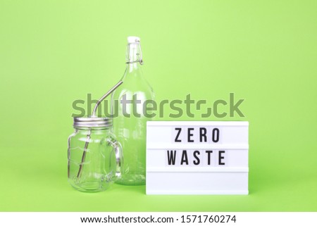 Reusable glass bottle and jar with metal straw and cinema lightbox showing Zero Waste text on the light green drop