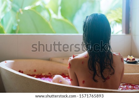 Back view of Woman relaxing in round outdoor bath with tropical flowers, organic skin care, luxury spa hotel, lifestyle photo