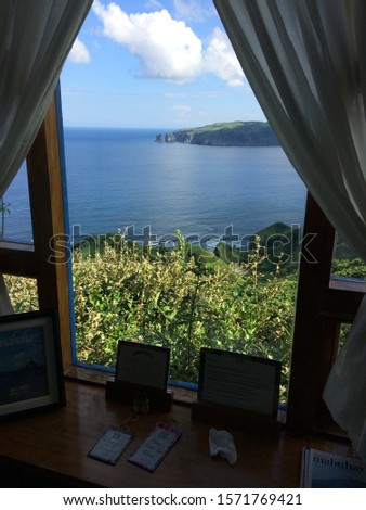 A vertical shot of a window with pictures near it and a view of the sea under a blue sky at daytime