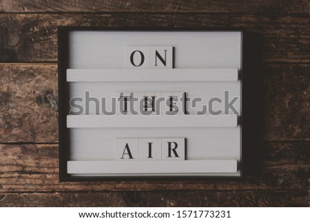 A white sign with writing "On the air" on it on a wooden brown background